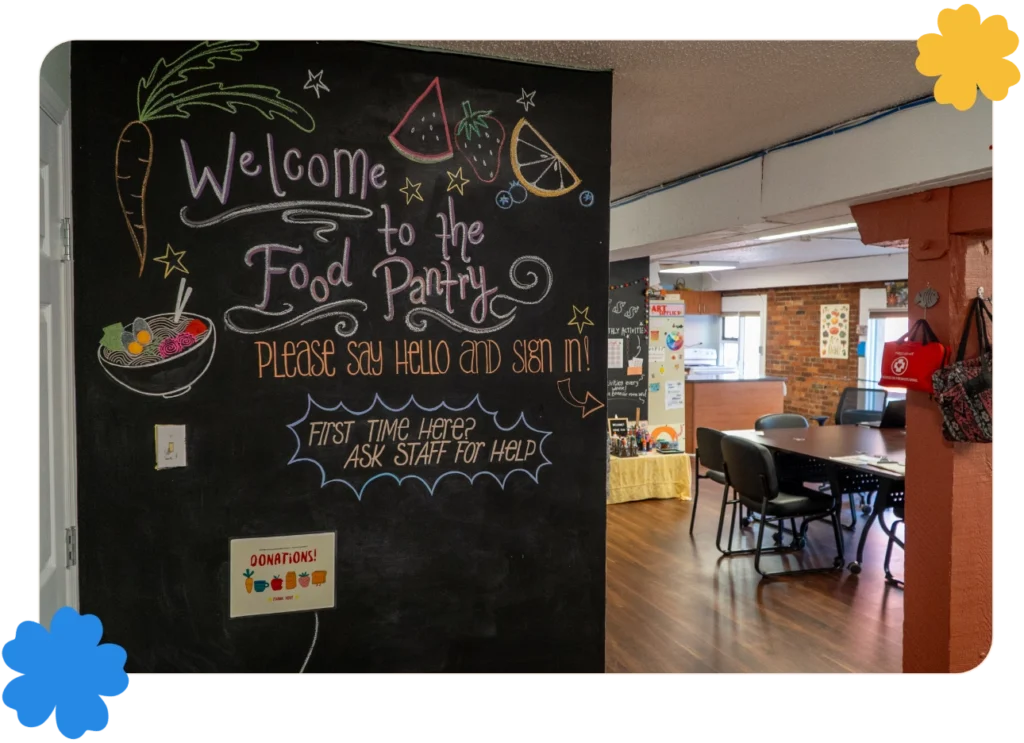 A photo of the entrance to the VYES Food Pantry. The blackboard reads "Welcome to the Food Pantry. Please Say Hello and Sign In. First Time Here? Ask Staff for Help".