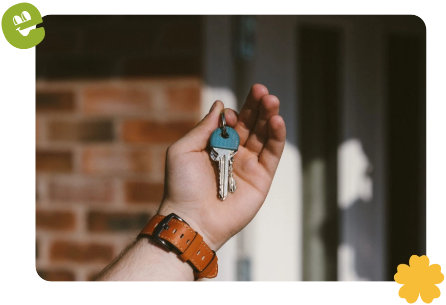 A hand holds a set of keys in front of a building door.