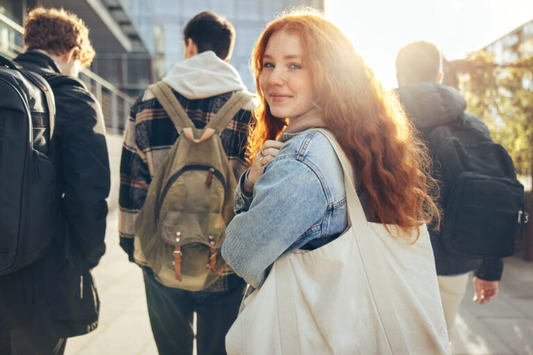 A group of young people is walking away from the camera. A young woman turns towards the camera with a smile.