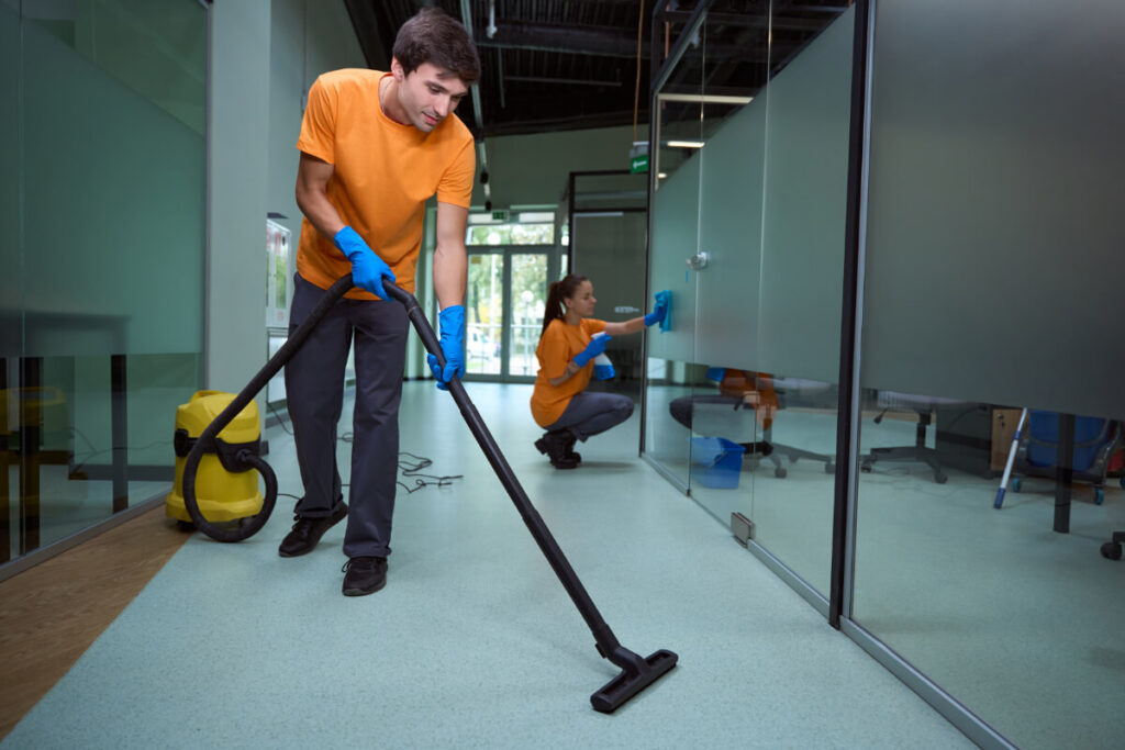 A young man and women wearing orange uniforms clean an office building hallway.