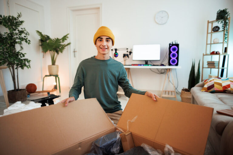 A smiling young man is unpacking a box in his apartment