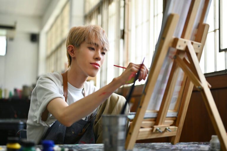An LGBTQ artist with colored hair doing artwork in a workshop studio.