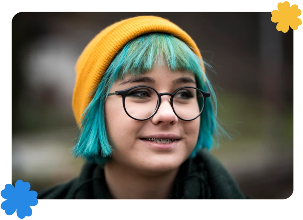 Young smiling girl with died green/blue hair, yellow cap and eyeglasses.