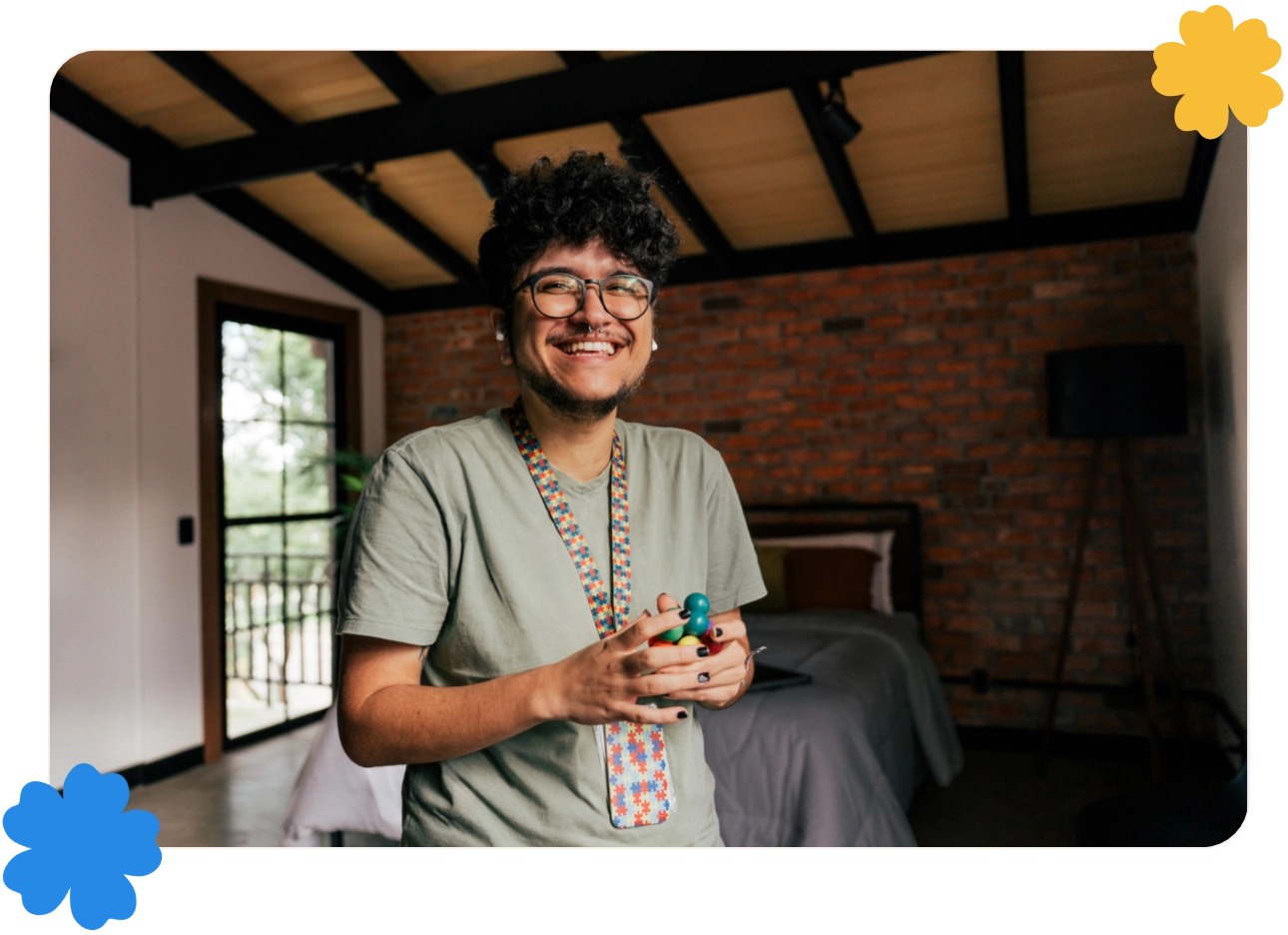 A smiling young man stands in bedroom. He is holding a fidget toy.