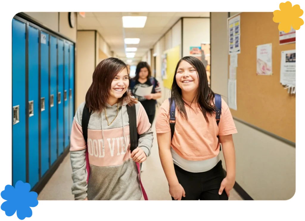 Two school girls walking down the school corridor and smiling in front of lockers.